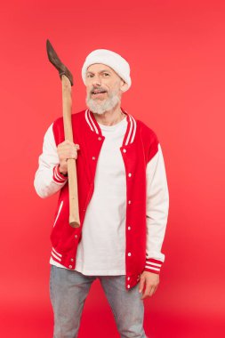 Orta yaşlı, Noel Baba şapkalı, elinde baltayla kırmızı bir adam.