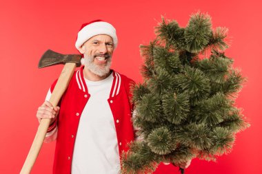 Noel Baba şapkalı mutlu orta yaşlı bir adam elinde balta ve kırmızı üzerinde çam ağacı tutuyor.