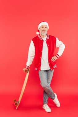 Noel Baba şapkalı orta yaşlı adam bacak bacak üstüne atmış ve kırmızı kaykaylı.