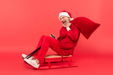 Noel Baba şapkalı ve takım elbiseli, kırmızı kızakla kızak süren orta yaşlı bir adam.