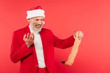 Noel Baba şapkalı olgun bir adam kırmızı üzerine izole edilmiş el işi kağıdında mektup okuyor.