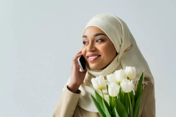 Счастливая Мусульманка Хиджабе Держа Букет Тюльпанов Разговаривая Смартфоне Изолированном Сером — стоковое фото