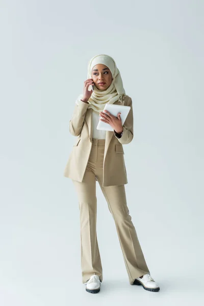 全身上下都是年轻的穆斯林女性 头戴头巾 手持数码平板电脑 用灰色手机聊天 — 图库照片