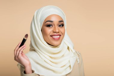 tesettürlü mutlu müslüman kadın elinde kozmetik fırça bej üzerinde izole edilmiş