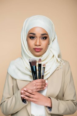 tesettürlü genç müslüman kadın bej üzerine izole edilmiş kozmetik fırça setini tutuyor