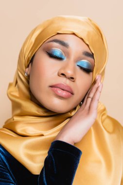 Parlak mavi göz makyajlı, bej renkli kapalı gözlü, tesettürlü Müslüman kadın.