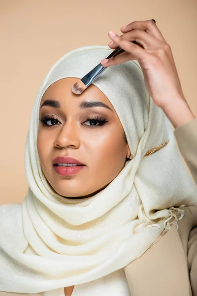 Junge Muslimin Hijab Trägt Gesichtsfundament Mit Kosmetikbürste Isoliert Auf Beige — Stockfoto