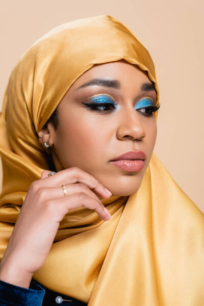 muslim woman in hijab with bright makeup looking away isolated on beige