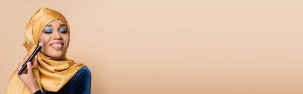 Щаслива Мусульманка Жовтому Хіджабі Наносить Макіяж Фундаменту Косметичним Пензлем Ізольовано — стокове фото
