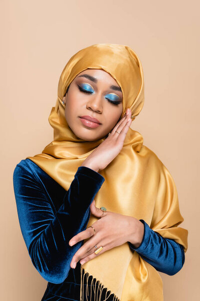 young muslim woman in yellow hijab posing with closed eyes isolated on beige