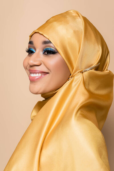 happy muslim woman in yellow hijab smiling isolated on beige