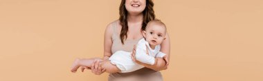 Smiling woman holding baby girl isolated on beige, banner  clipart