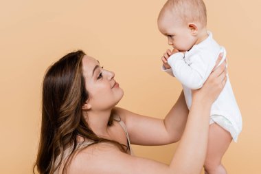 Aşırı kilolu bir kadının bej üzerinde izole edilmiş bebeğe bakışı 