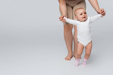 Gri arka planda gülümseyen kızının elini tutan pozitif anne.