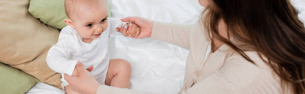 High angle view of mother holding hands of baby daughter on bed at home, banner 