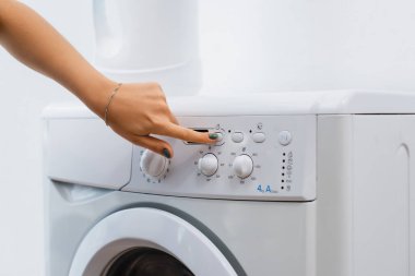 Çamaşır makinesindeki düğmeye basan ev kadınının kırpılmış görüntüsü