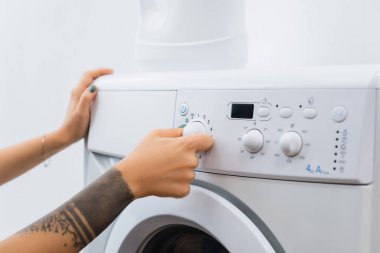 Dövmeli bir kadının evde çamaşır makinesi kullanması.