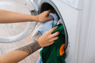 Çamaşırları çamaşır makinesine koyan dövmeli kadının kısmi görüntüsü
