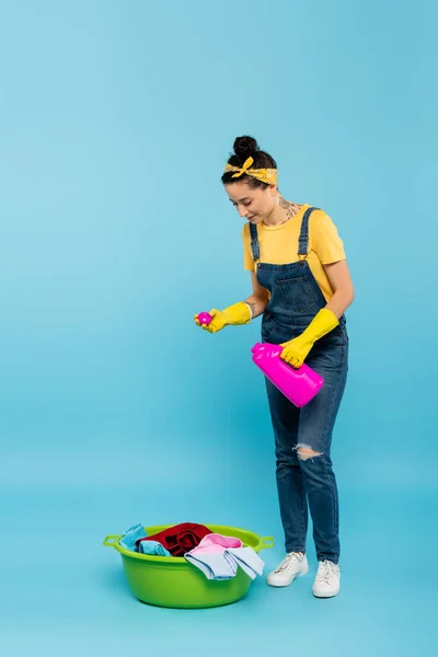 Młoda Gospodyni Domowa Dżinsowych Kombinezonach Wlewając Detergent Miski Pranie Niebiesko — Zdjęcie stockowe