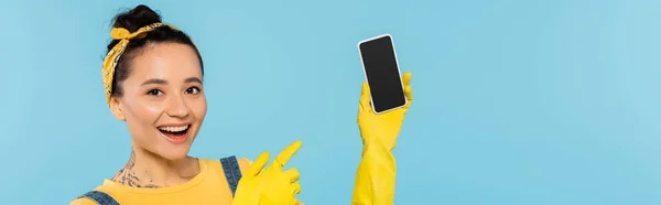 穿着黄色橡胶手套的快乐女人指着笔记本电脑 屏幕空白 蓝色横幅隔离 — 图库照片