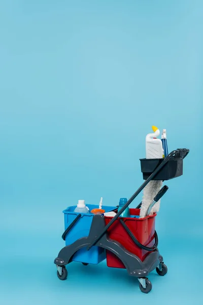 Wagen Mit Verschiedenen Reinigungsmitteln Und Eimern Auf Blauem Hintergrund — Stockfoto