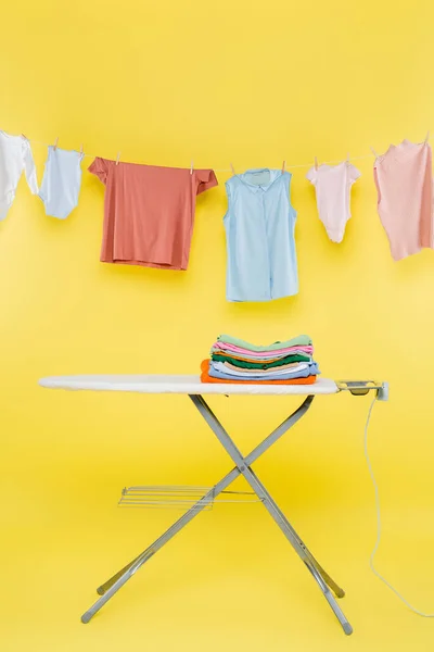 Stack Clean Clothes Ironing Board Laundry Hanging Rope Yellow Background — Stock Photo, Image