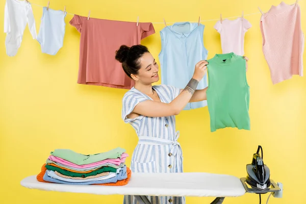 Mujer Sonriente Sosteniendo Camisa Sin Mangas Cerca Tabla Planchar Amarillo —  Fotos de Stock