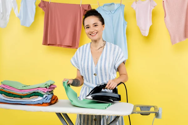 Brunette Woman Smiling Camera While Ironing Clothes Hanging Laundry Yellow — Stock Photo, Image