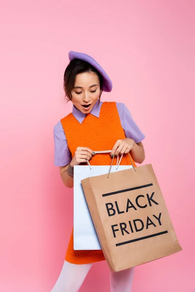 穿着紫色贝雷帽的女人惊讶地看着购物袋 上面有黑色星期五的字母 粉色孤立 — 图库照片
