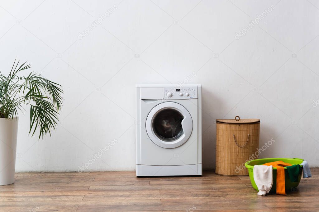 laundry bowl, basket and washing machine near green plant and white wall