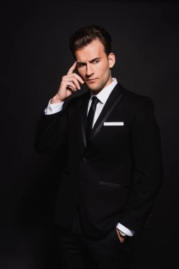 Zarif takım elbiseli düşünceli bir adam elini cebine atarak başını okşuyor.