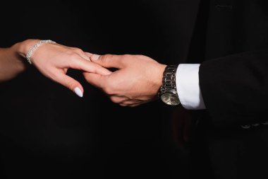 cropped view of man in wristwatch holding hand of woman in bracelet isolated on black clipart