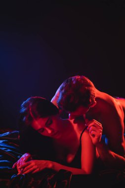 Genç üstsüz adam siyah arka planda kırmızı ışıklı seksi kadına sarılıyor.