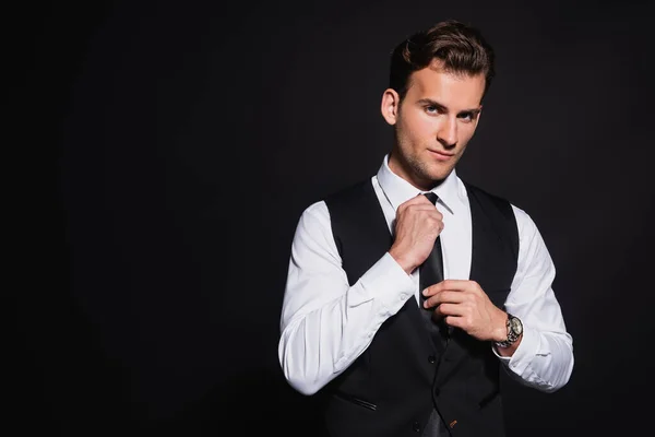 Young Stylish Man Looking Camera While Touching Tie Isolated Black — Stock Photo, Image