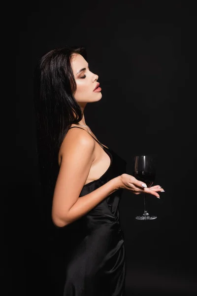 从侧面看穿着缎子衣服的性感女人 她的姿势是闭着眼睛 喝着红葡萄酒 与黑色隔离 — 图库照片