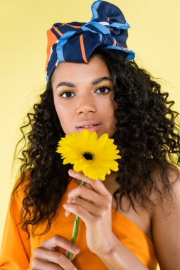 Sarı renkte çiçek tutan Afro-Amerikan kadın.