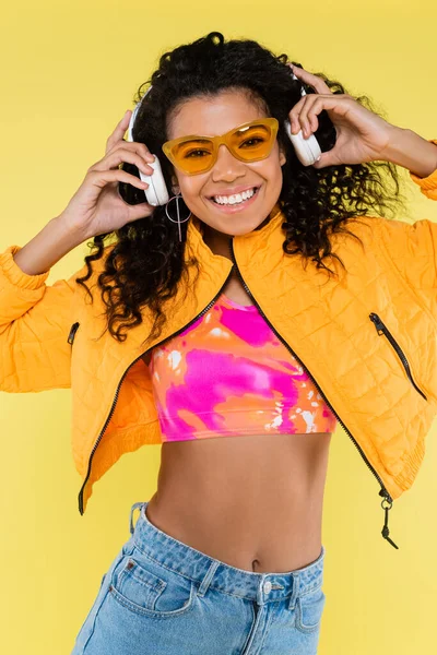 幸せなアフリカ系アメリカ人の若い女性が黄色で隔離されたヘッドフォンを調整して — ストック写真