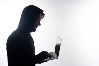 Gri ekranda boş ekranı olan bir dizüstü bilgisayar kullanan başlıklı hacker yan görünümü 