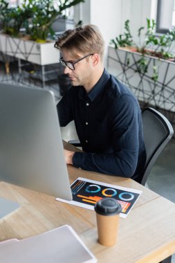 Gözlüklü programcı belgenin yanında bilgisayar ve ofiste kahve kullanıyor. 