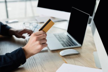 Ofiste boş ekranlı bilgisayarların yanında kredi kartı tutan programcı görüntüsü 