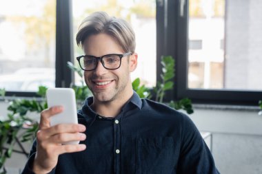 Ofiste bulanık akıllı telefon kullanan gözlüklü genç programcı. 