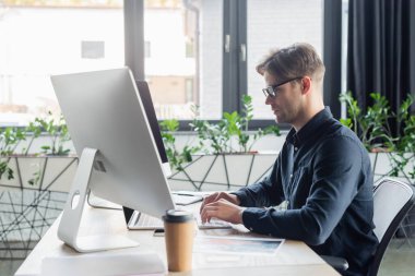 Ofiste bulanık belge ve kahve yanında bilgisayar kullanan programcının yan görünümü 