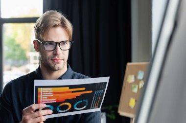 Genç programcı ofisteki bulanık çevirme çizelgesinin yanında belge tutuyor 