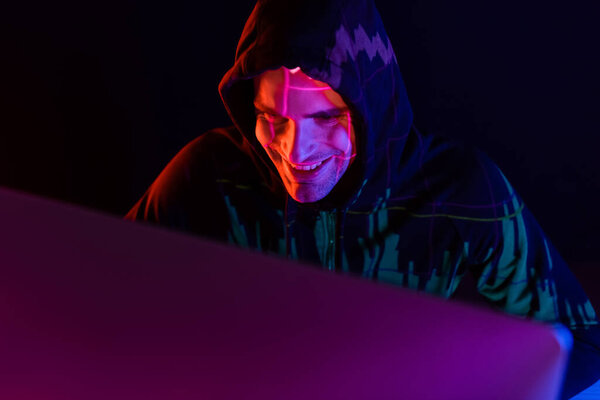 Smiling hacker with reflection of charts using computer isolated on black 