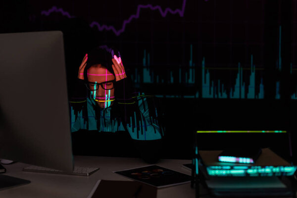 Upset hacker with charts reflection sitting near computer and documents on black background 