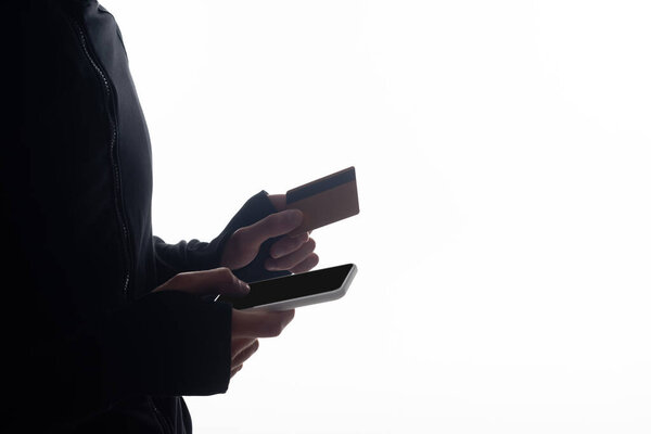 Cropped view of hacker using smartphone and holding credit card isolated on white 