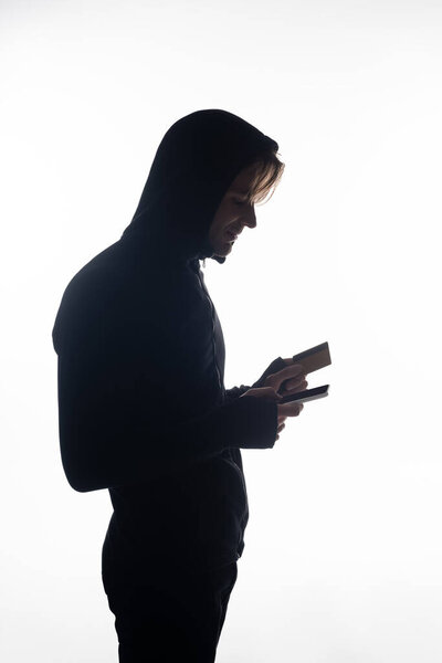 Side view of hacker holding cellphone and credit card isolated on white 