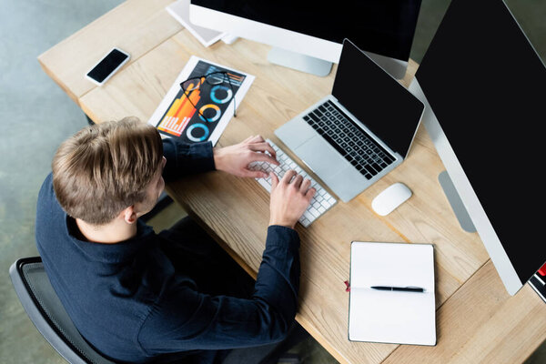 Overhead view of programmer using computers near smartphone and eyeglasses on table 
