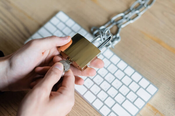Cropped view of programmer holding padlock and key near keyboard in office 