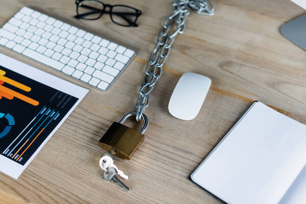 Padlock on chain near paper with graphs and keyboard in office 